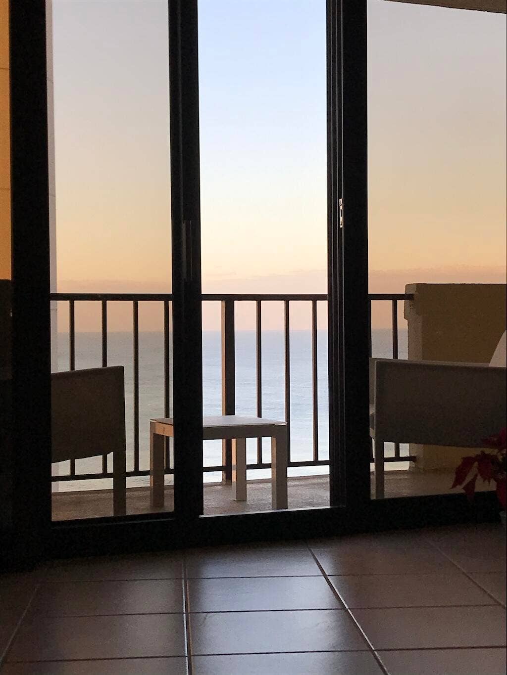 Sliding glass doors opening to a balcony with black metal railings, overlooking a body of water