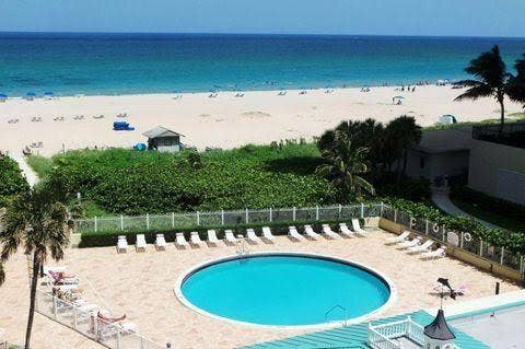 Circular swimming pool with surrounding lounge seating, paved pool deck, and palm trees