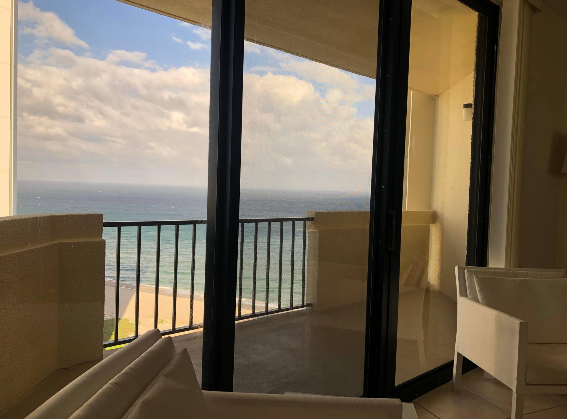 Full-height sliding glass doors opening to a balcony with ocean and beach scenery