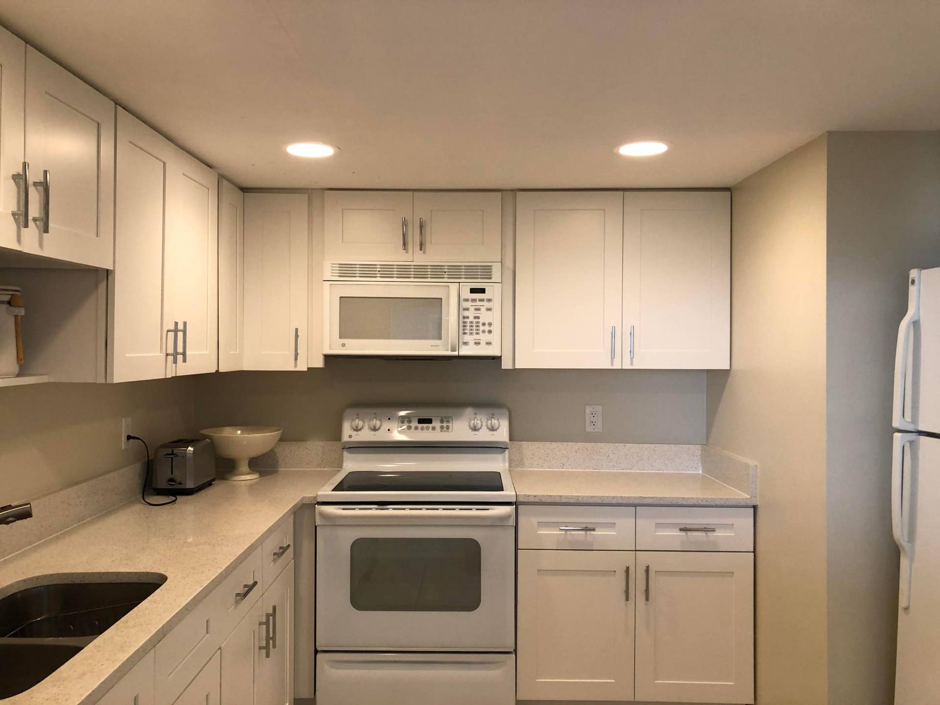 White shaker-style cabinetry with chrome hardware, light-toned countertops, stainless steel undermount sink, and recessed lighting