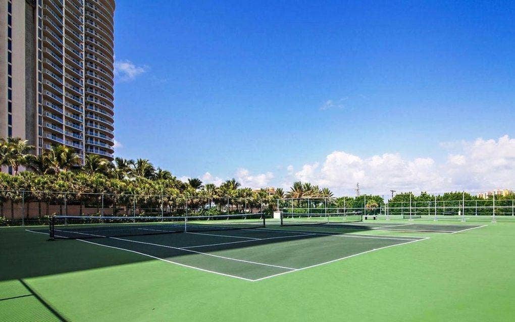 Professional-grade tennis courts featuring hard court surfaces with regulation net systems, surrounded by mature palm landscaping and high-fencing