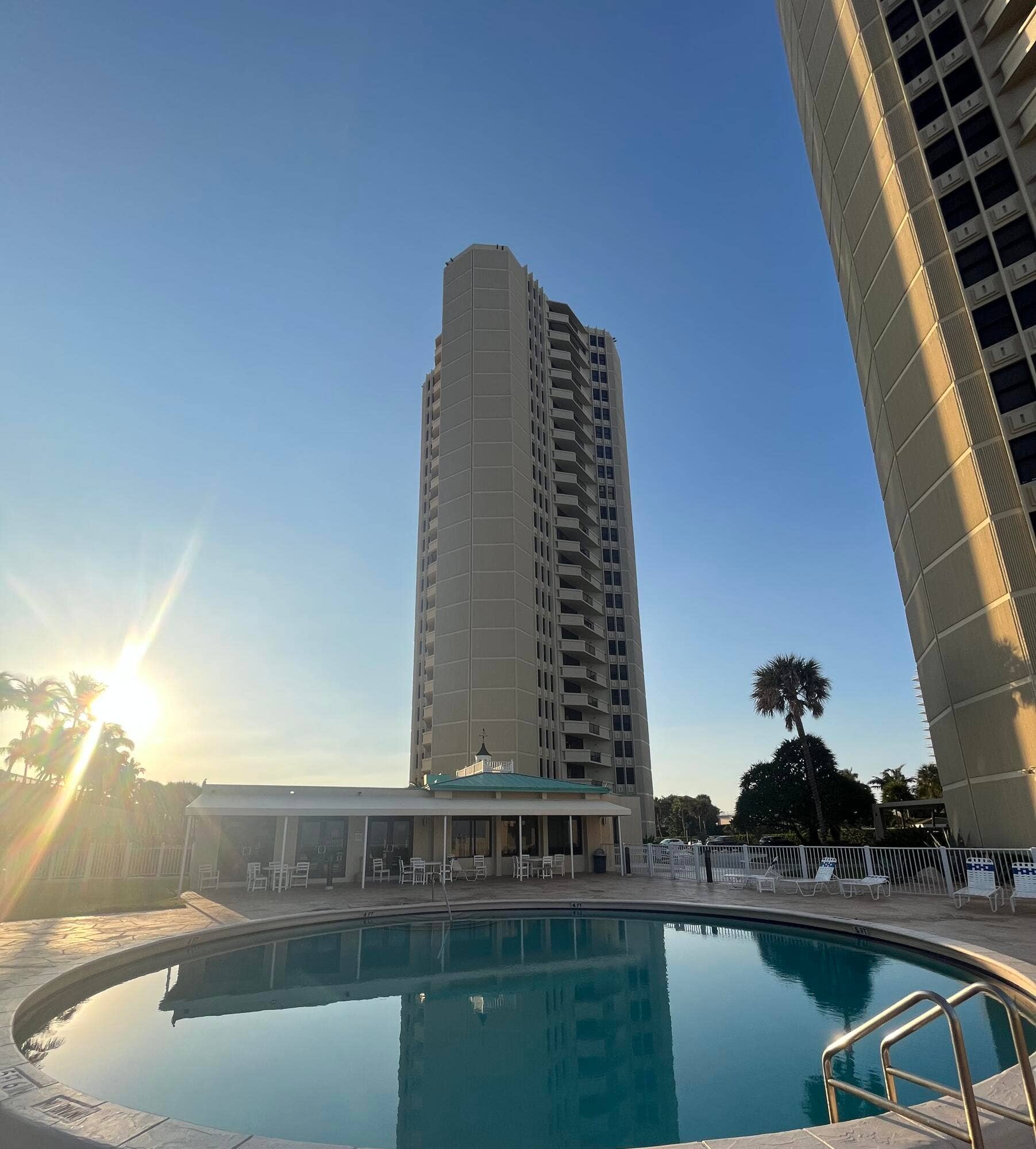Outdoor pool with a surrounding patio, adjacent to a multi-story building featuring private balconies