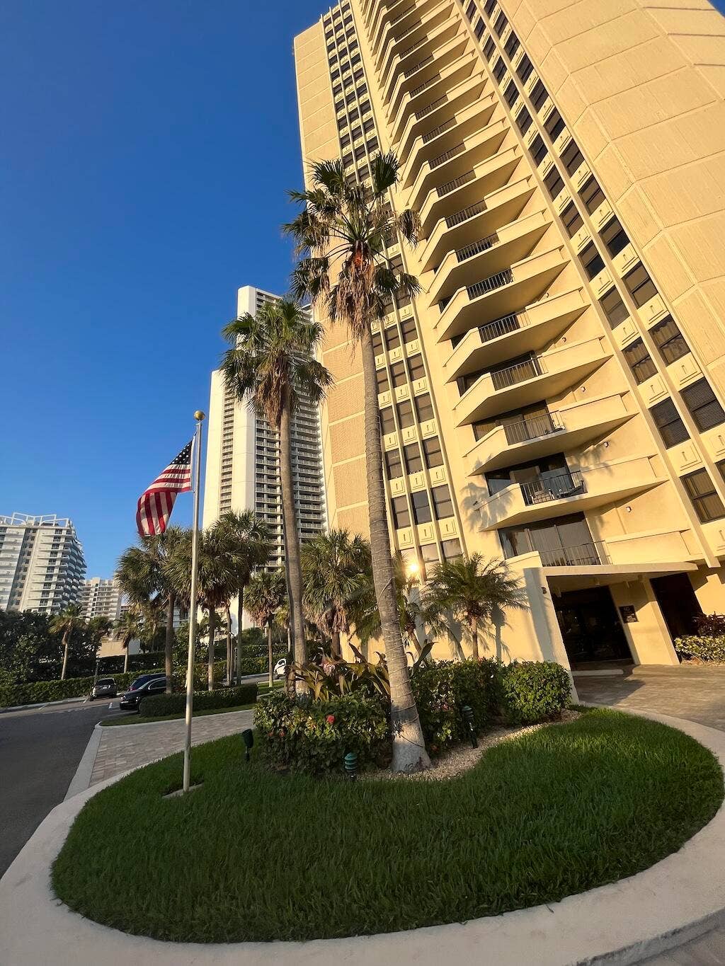 High-rise building with numerous balconies, featuring lush landscaping and mature palm trees