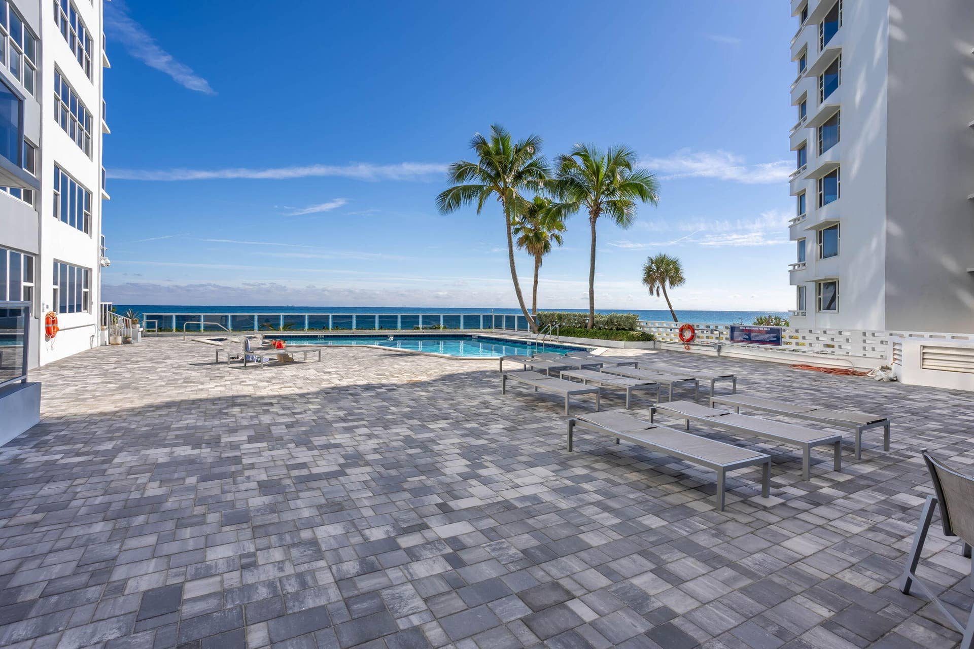 Expansive pool area with lounge chairs, dining tables, tiki hut with 2 BBQ grills and private resident beach access