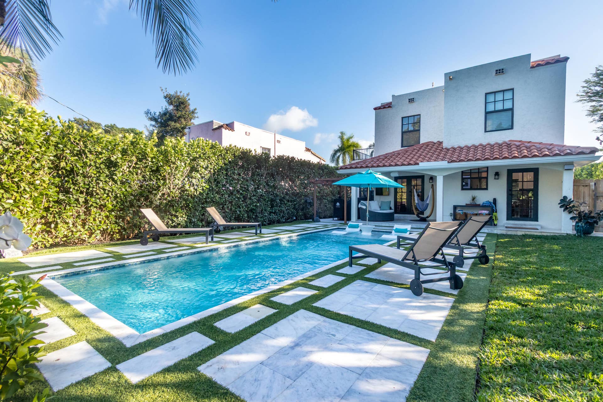 Backyard oasis with heated salt-water pool, covered loggia, stone pavers, lush landscaping, synthetic turf, & impressive surround sound