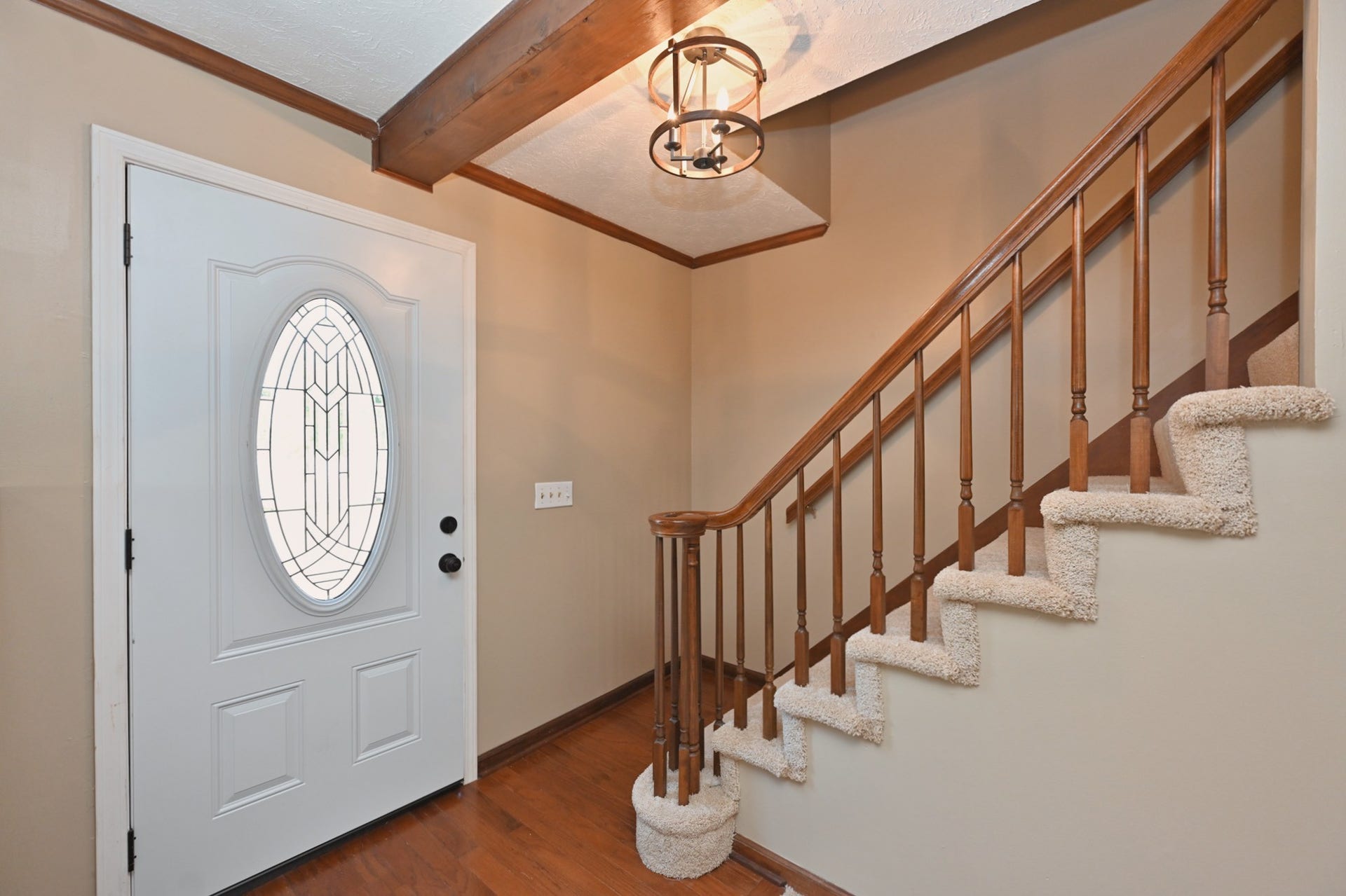 entryway with hardwood flooring and freshly carpeted stairs