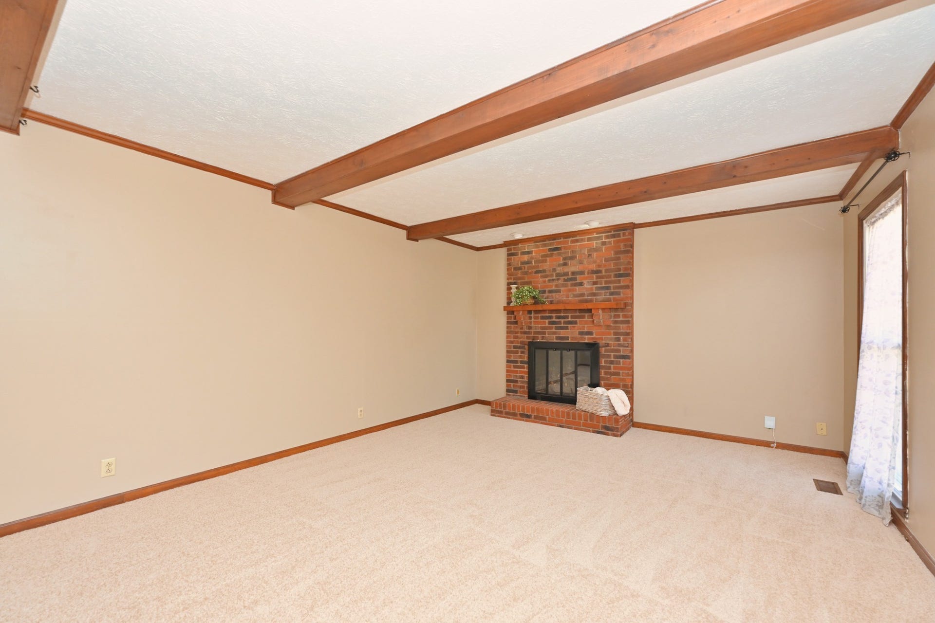 Spacious living area with wood beams and brick gas fireplace with beautiful logs