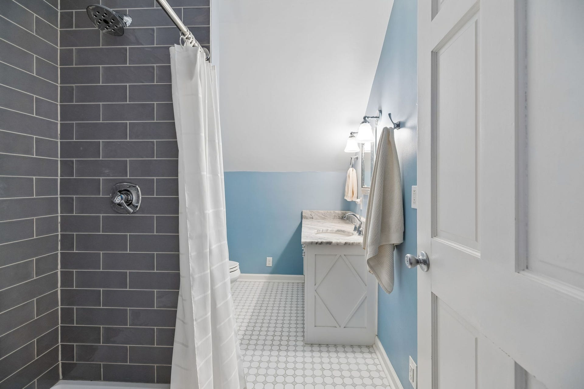 Even the upstairs bath has its own personality. Crisp white cabinetry and a marble-look countertop meet a classic tile shower and patterned floor, creating a space that feels fresh, cheerful, and thoughtfully finished.