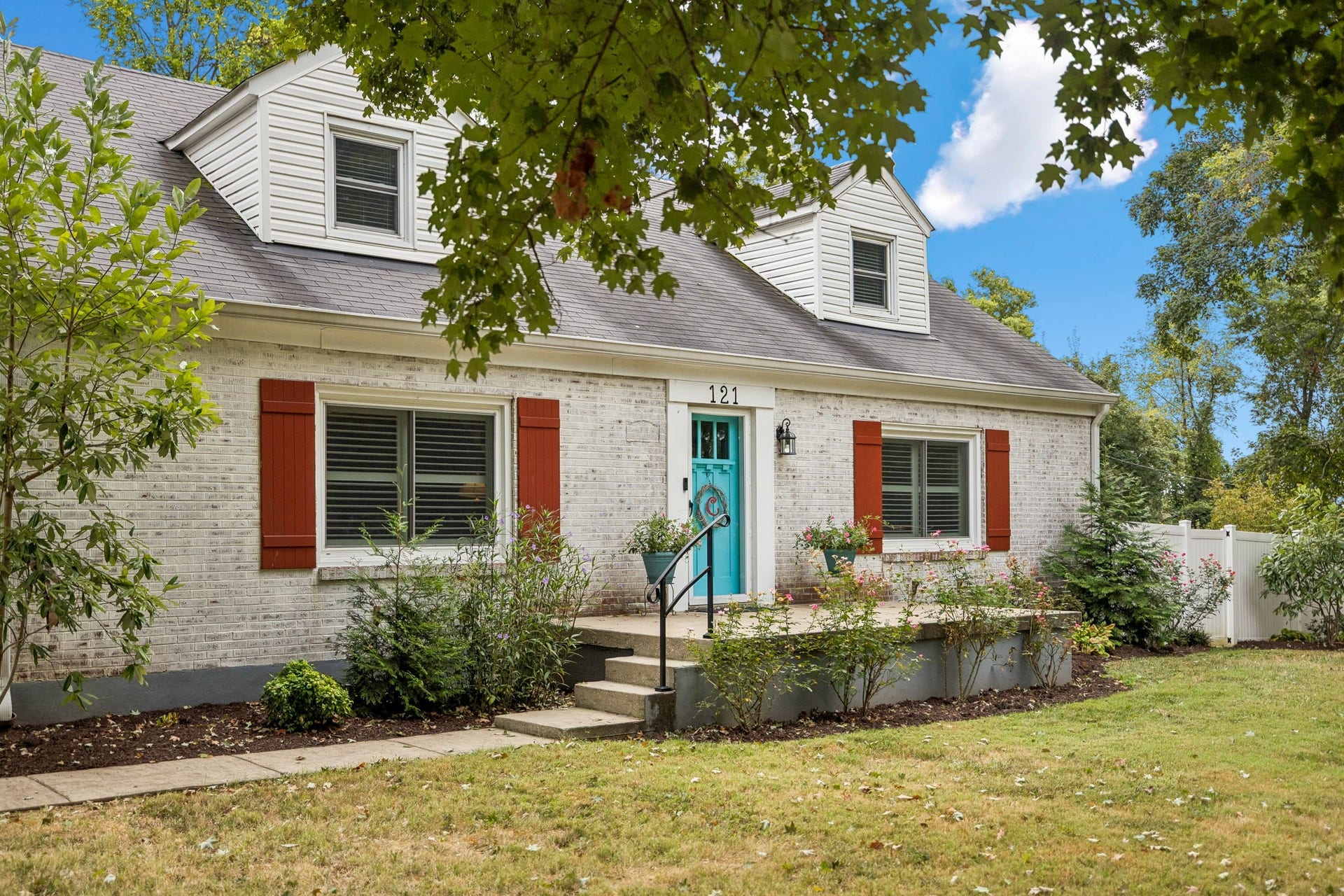 Its hard not to fall for a house like this. White brick, classic shutters, mature landscaping, and that unmistakable turquoise door give this storybook cottage its personality before you even step inside.