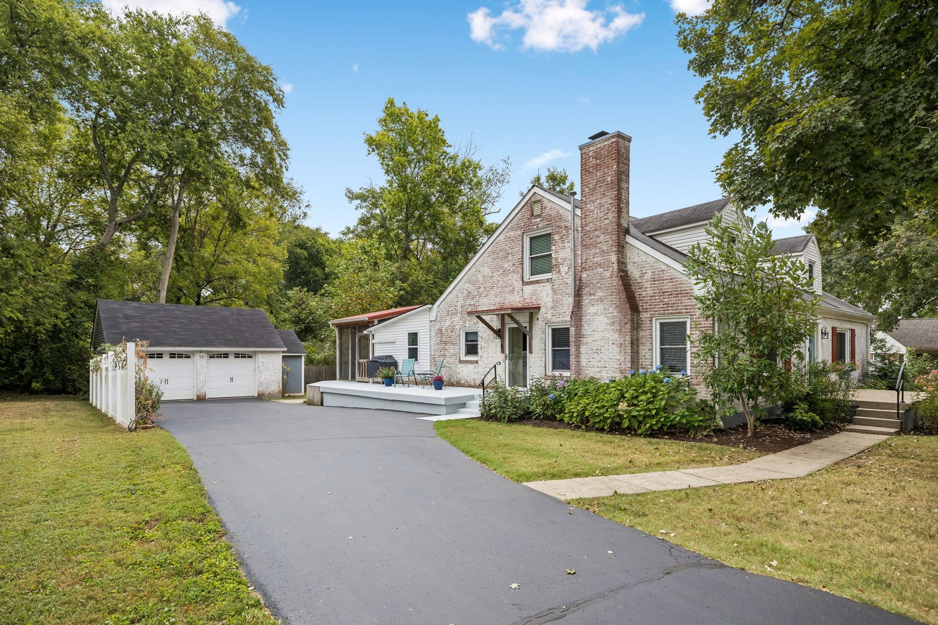 Around back, the story continues. Mature trees create a private backdrop, while the detached garage and expansive driveway add flexibility and functionality.