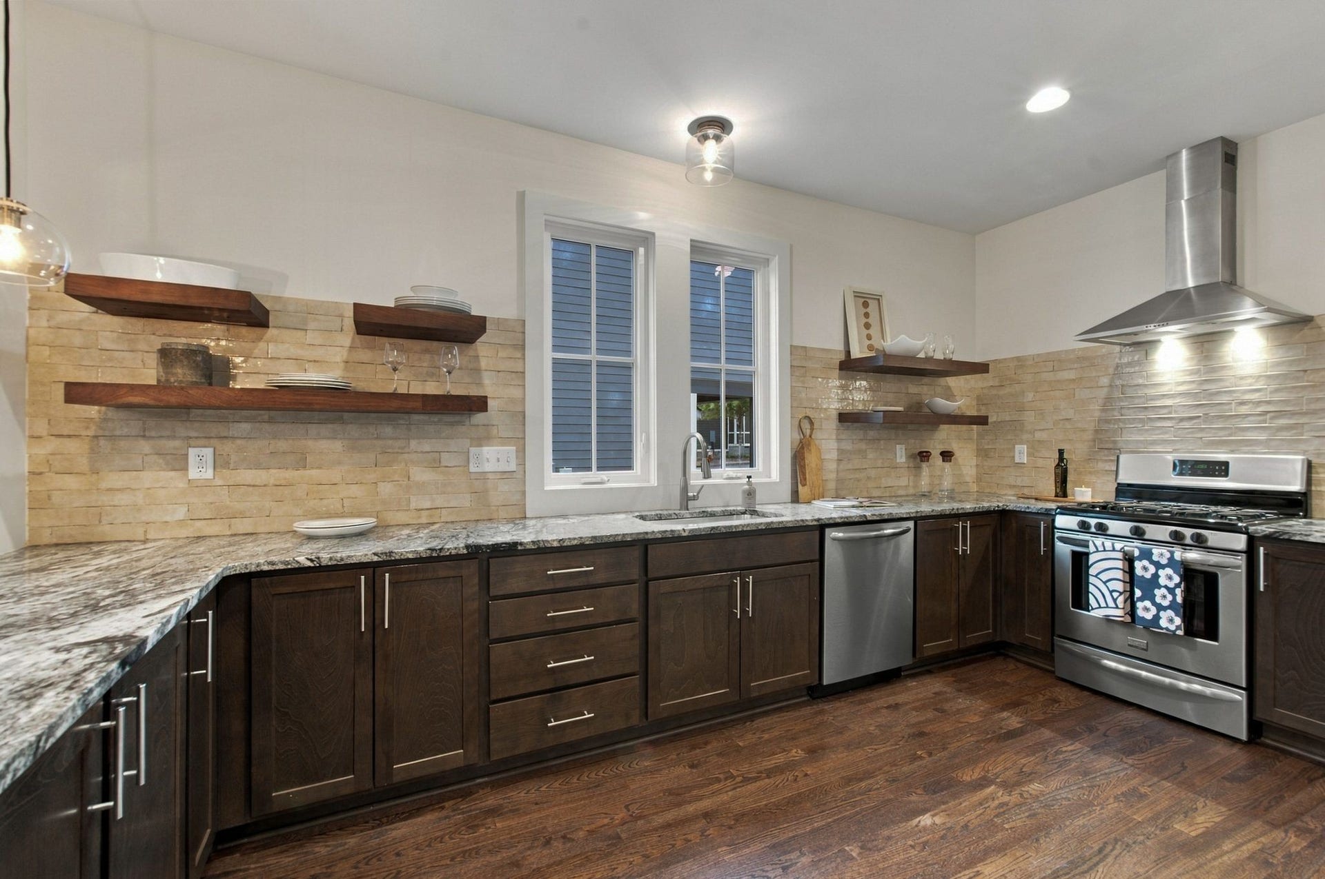 The kitchen has a gas range, vent hood, floating shelves and a lovely tiled backsplash