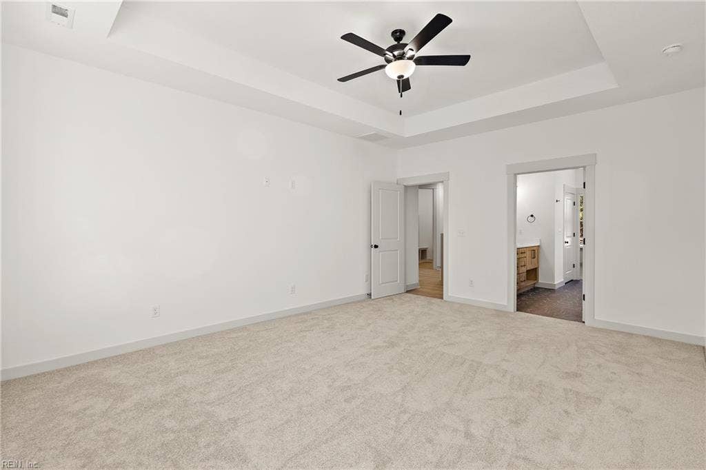 1st Floor Owner's Suite.The 1st Floor Owner's Suite offers a tray ceiling, ceiling fan with light, carpeting, ensuite bath, and large walk in closet with wood shelving.