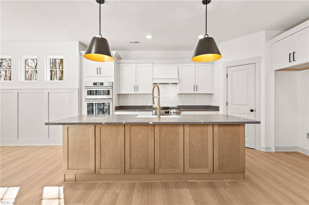 Eat in Kitchen. The Eat in Kitchen offers a center island with overhang for additional seating, pendant & recessed lighting, large dining area with chandelier, apron sink and goose neck faucet, soft close custom cabinets, quartz counters, ceramic tile backsplash, & walk in pantry w/ wood shelving.