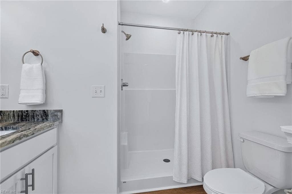 Primary bathroom with LVP flooring, double vanity with granite counters and walk in shower