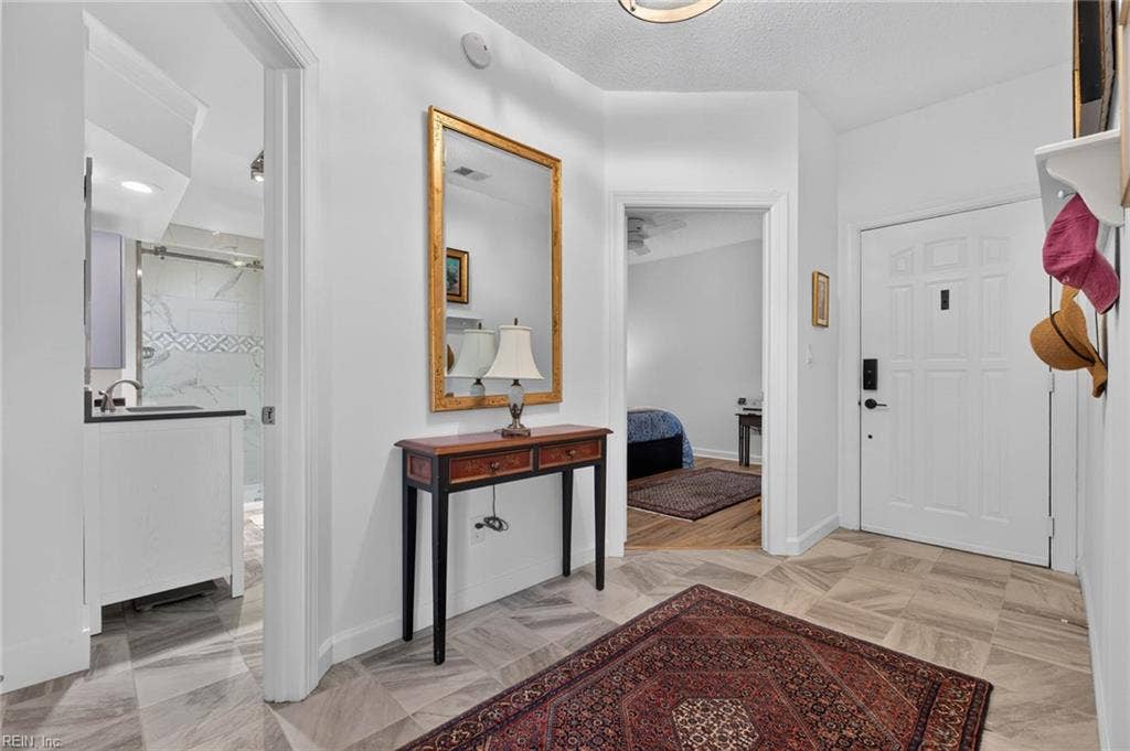 Entry foyer with tile floor and keypad door lock, with views to the hall bathroom with sliding glass shower door and a bedroom with ceiling fan. 1,555 sq ft first-floor condo at Lesner Pointe, Chic's Beach, Virginia Beach.