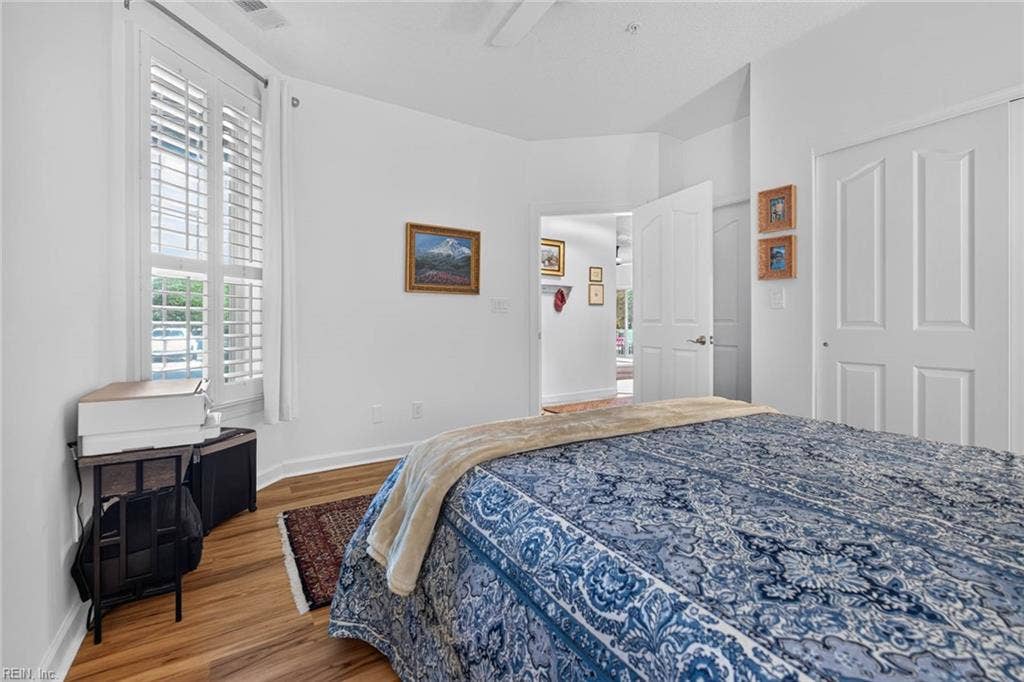Second bedroom with tall plantation-shuttered window, ceiling fan, double-door closet, and LVP flooring. Door opens to the entry foyer of this first-floor Lesner Pointe condo, 1,555 sq ft, in Chic's Beach, Virginia Beach.
