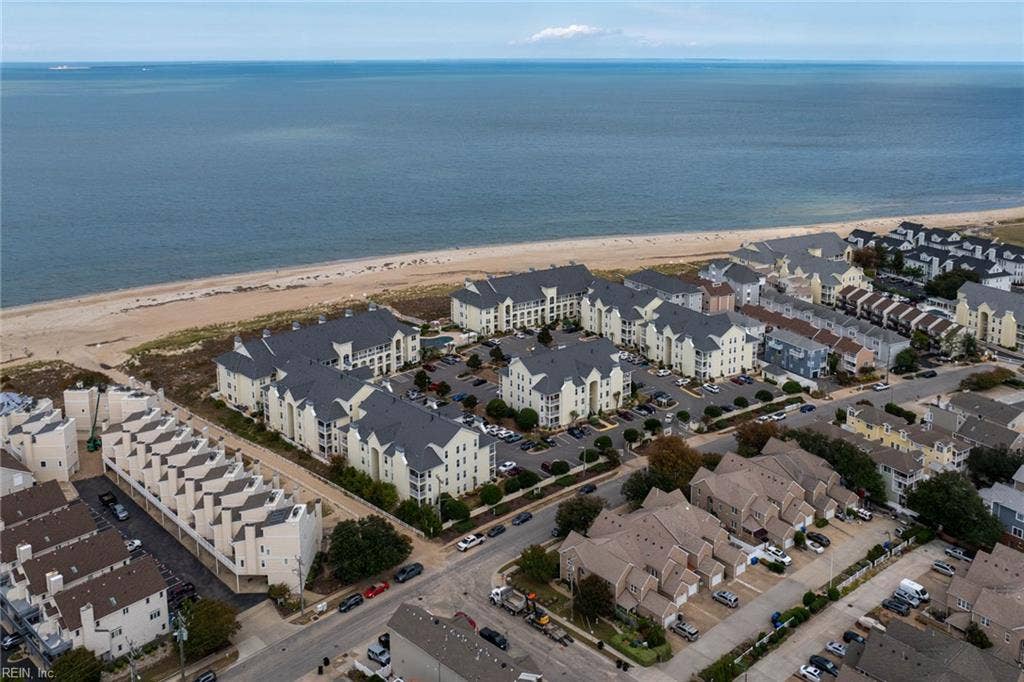 Aerial view of the Lesner Pointe condominium community between the Chesapeake Bay beach and the residential streets of Chic's Beach, Virginia Beach. Community parking sits beside the buildings, with the pool near the dunes. 23451.