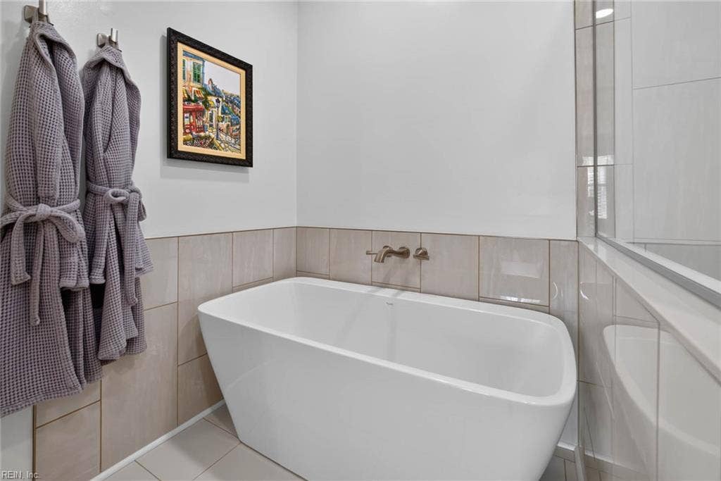 Primary bathroom freestanding soaking tub with wall-mounted faucet and tile surround, next to the glass-enclosed shower. Gutted and renovated by current owners with a new standalone tub. Lesner Pointe condo, Chic's Beach, Virginia Beach.