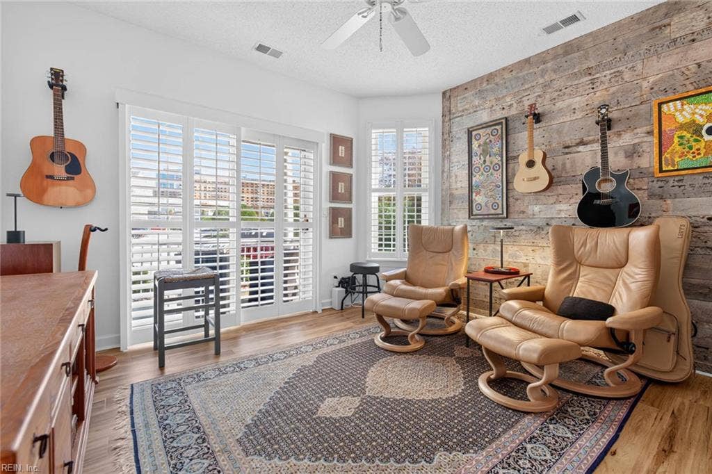 Den with reclaimed wood accent wall, ceiling fan, LVP flooring, and plantation-shuttered sliding glass door to the covered porch. Flexible room works as a third bedroom, home office, or workout room. First-floor Lesner Pointe condo, Chic's Beach, Virginia Beach.
