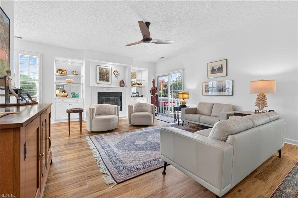 Living room with gas fireplace, built-in shelving, ceiling fan, and LVP flooring in this 1,555 sq ft first-floor condo at Lesner Pointe, Virginia Beach. Plantation shutters and a sliding glass door to the covered patio bring in natural light.
