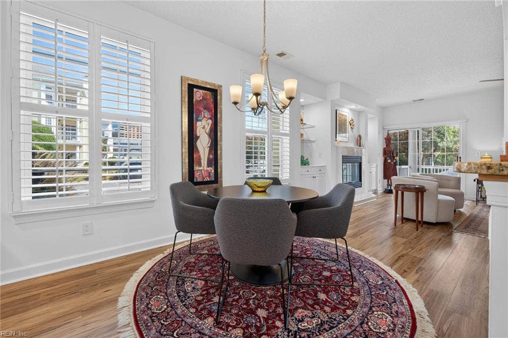 Dining area with chandelier and large plantation-shuttered windows that bring in natural light, open to the living room and fireplace. Located in this 3 bedroom, 2 bath first-floor condo at Lesner Pointe, Chic's Beach, Virginia Beach.