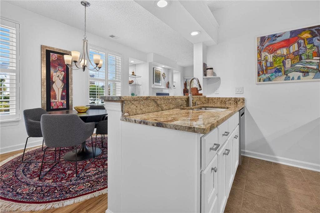 Kitchen with granite countertops, double stainless sink, pull-down faucet, dishwasher, and a raised bar counter open to the dining area. White cabinets and tile flooring in this Lesner Pointe condo, Chic's Beach, Virginia Beach.
