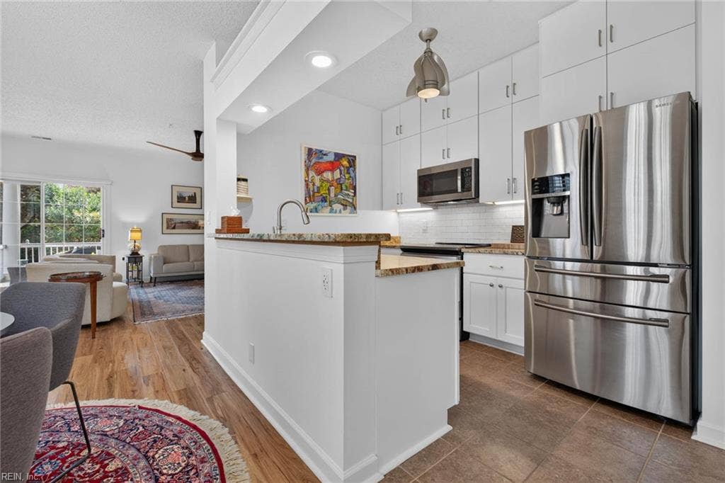 Kitchen with granite countertops, white cabinets to the ceiling, subway tile backsplash, stainless appliances, and under-cabinet lighting. Raised bar counter opens to the living room in this Lesner Pointe condo, Chic's Beach, Virginia Beach.