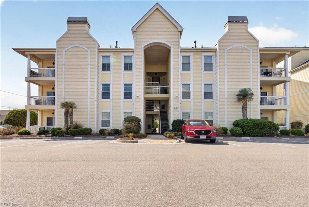 Front of the 3159 Silver Sands Circle building at Lesner Pointe in Chic's Beach, Virginia Beach, with arched central entry, covered porches, and parking lot in front. Unit 103 is on the first floor. 23451.