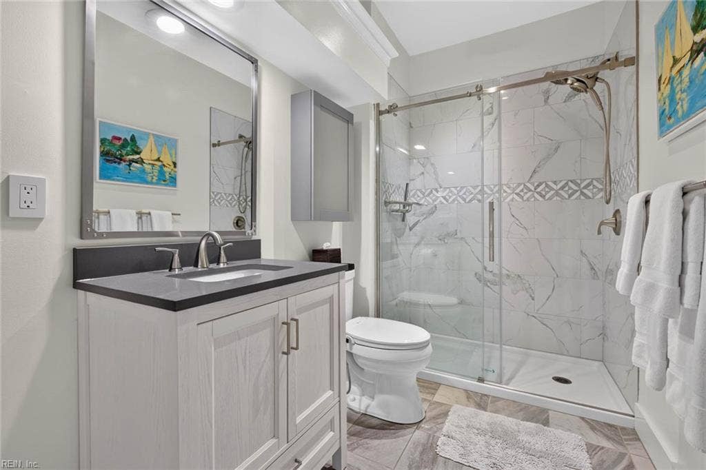 Hall bathroom with marble-look tile walk-in shower with sliding glass door, mosaic accent band, handheld shower, and single-sink vanity. Updated bath in this Lesner Pointe condo, Chic's Beach, Virginia Beach. 23451.