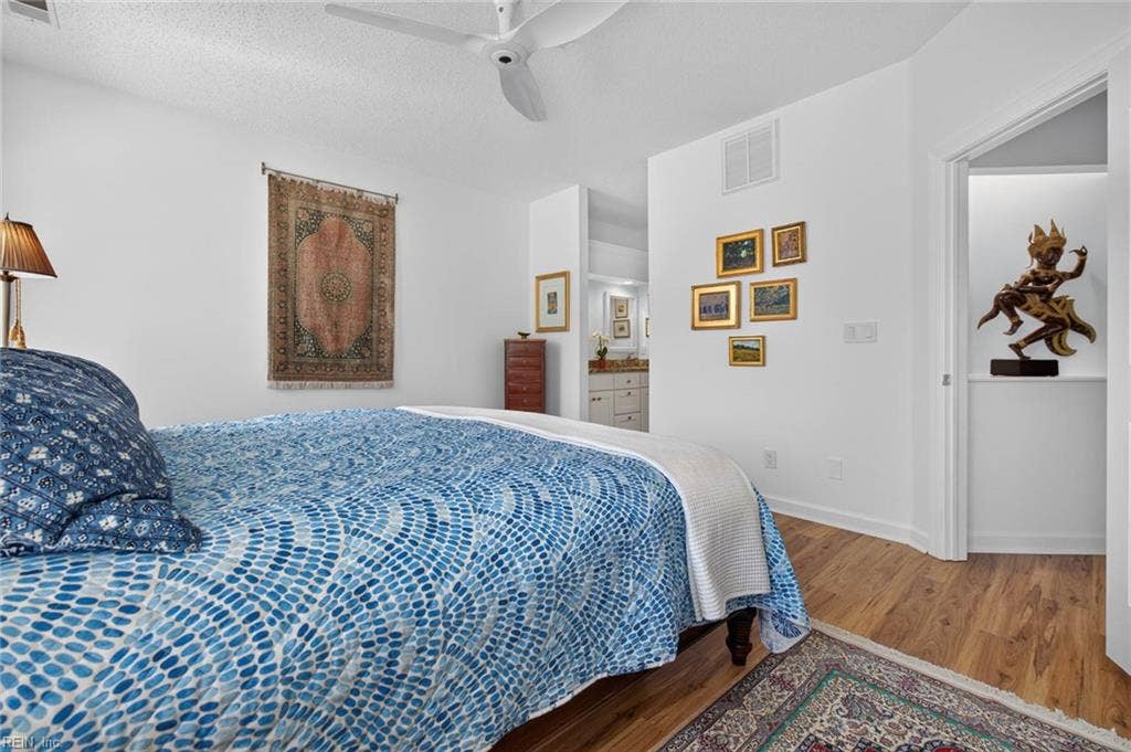 Primary bedroom with ensuite bath and walk-in closet access, ceiling fan, and LVP flooring. Dual-sink vanity visible through the bath entry. First-floor Lesner Pointe condo, 1,555 sq ft, in Chic's Beach, Virginia Beach.
