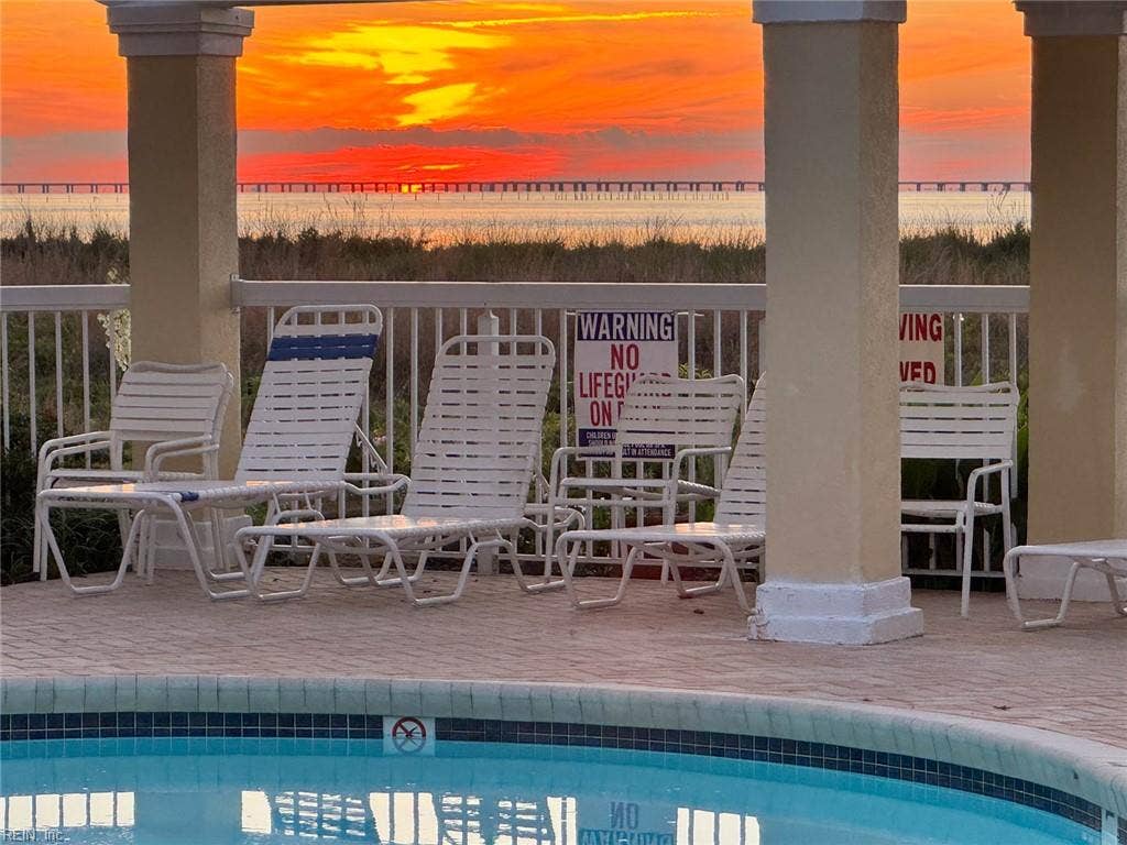 Sunset over the Chesapeake Bay from the Lesner Pointe community pool pergola in Chic's Beach, Virginia Beach, with the Chesapeake Bay Bridge-Tunnel on the horizon. Lounge chairs sit beside the pool. Pool access comes with the community.