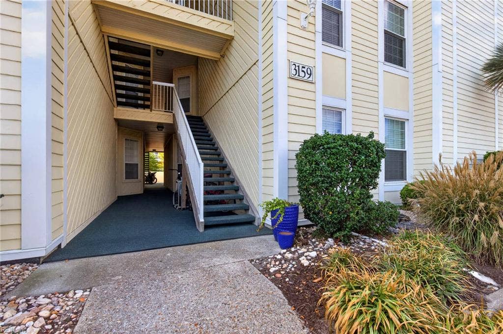 Covered ground-floor entry at 3159 Silver Sands Circle in Lesner Pointe, Chic's Beach, Virginia Beach, with a carpeted walkway and landscaped beds. First-floor condos in this building are entered at ground level. 23451.
