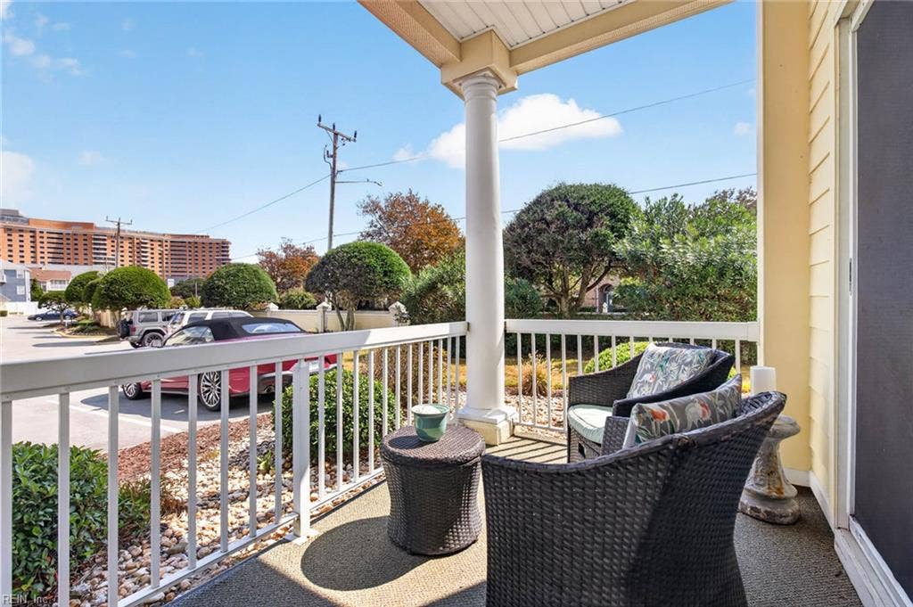 Covered porch with railing, column, and outdoor seating off the sliding glass door at this ground-level Lesner Pointe condo in Chic's Beach, Virginia Beach. Landscaped beds and the community parking area are in view. 23451.