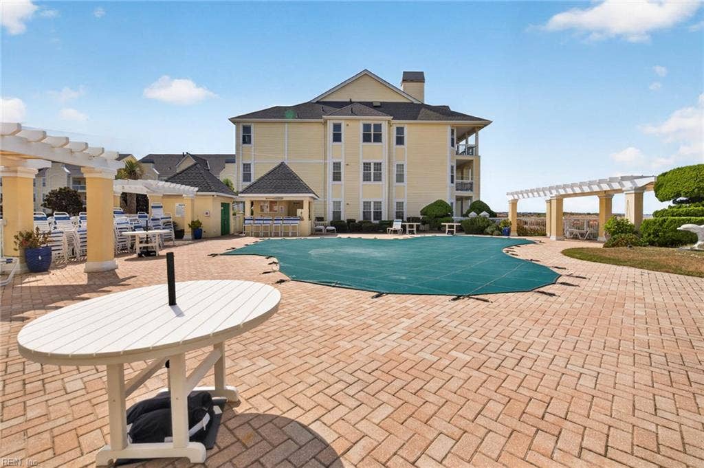 Lesner Pointe community pool deck with brick paver surface, pergola seating, covered cabana with bar seating, and lounge chairs in Chic's Beach, Virginia Beach. Pool shown with winter cover. Pool access comes with the community.