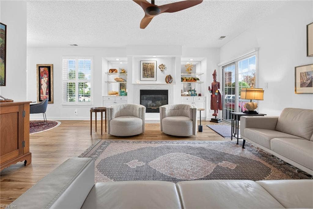 Living room with gas fireplace, lit built-in shelving and cabinets, plantation shutters, and a sliding glass door to the covered patio. LVP flooring in this 3 bedroom, 2 bath Lesner Pointe condo in Chic's Beach, Virginia Beach.