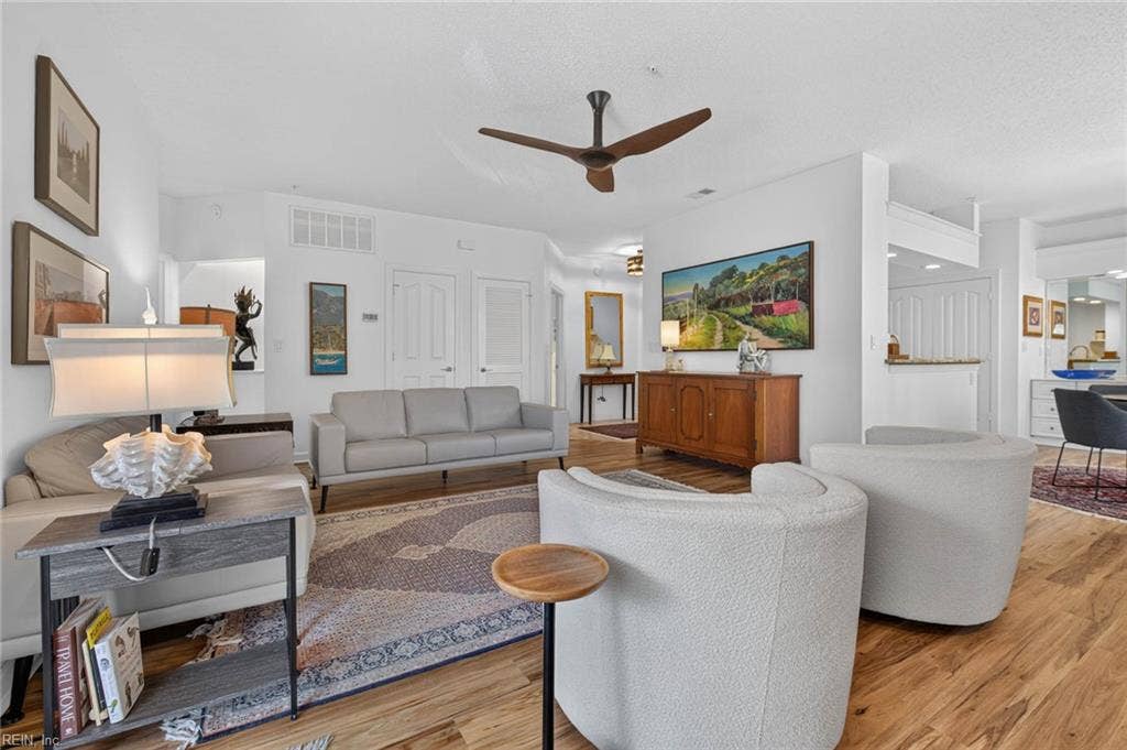 Living room seating area with ceiling fan and LVP flooring, looking toward the entry foyer in this first-floor condo at Lesner Pointe, Virginia Beach. Dining area and kitchen sit to the right in the same open layout. 1,555 sq ft.