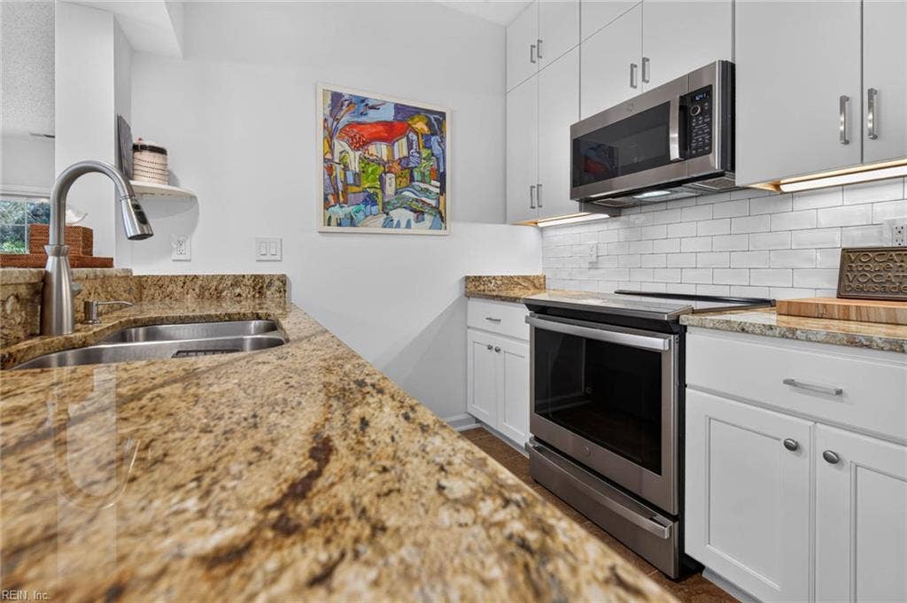 Kitchen with newer stainless appliances including range and over-the-range microwave, subway tile backsplash, under-cabinet lighting, and white cabinets to the ceiling. Granite countertops in this Lesner Pointe condo in Chic's Beach, Virginia Beach. 23451.