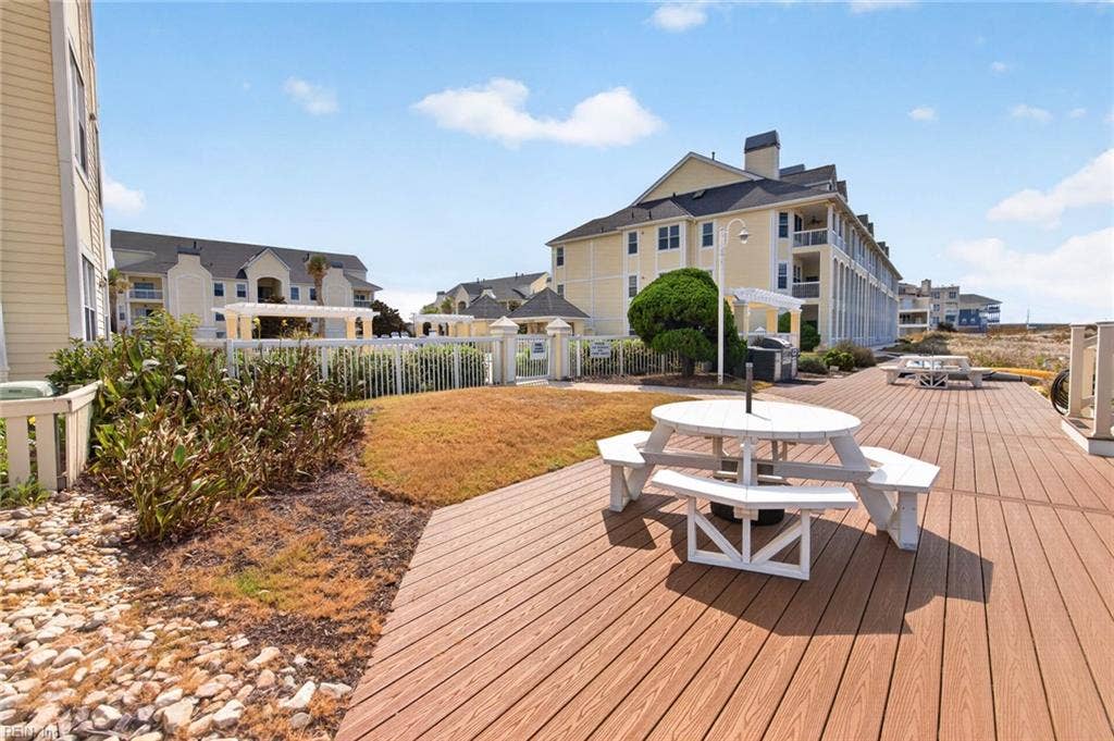 Community deck with picnic tables, grill area, and pool gate beside the dune walkway at Lesner Pointe in Chic's Beach, Virginia Beach. Outdoor gathering space sits between the condo buildings and the Chesapeake Bay beach.