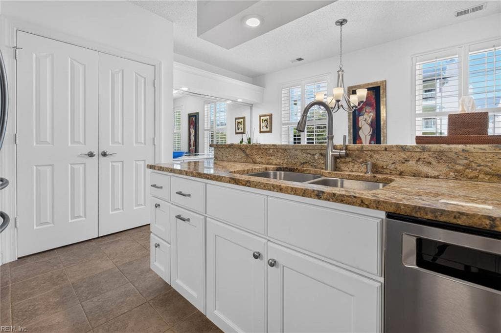 Kitchen with granite countertops, double stainless sink, pull-down faucet, stainless dishwasher, and white cabinets with drawers. Pantry and utility closet beside the kitchen. Open to the dining area in this Lesner Pointe first-floor condo, Chic's Beach, Virginia Beach.