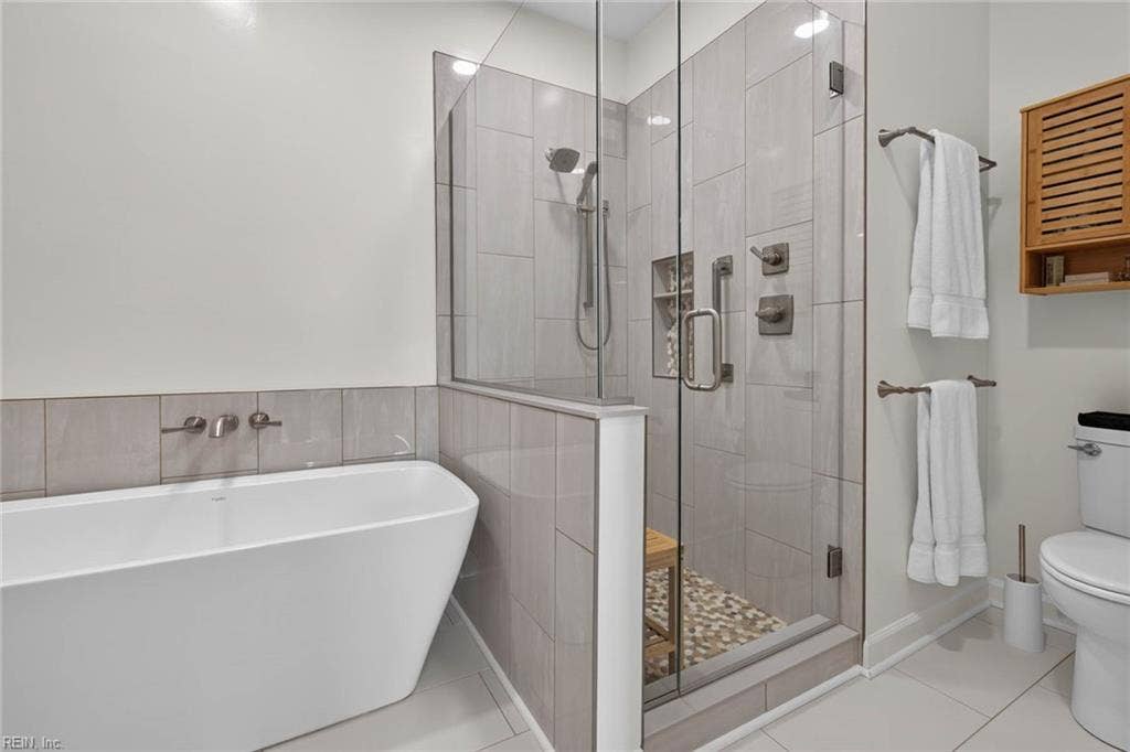Primary bathroom with freestanding tub, frameless glass shower with bench and pebble floor, and large-format tile. Fully renovated by the current owners with a new tub, shower, and tile. Lesner Pointe condo, Chic's Beach, Virginia Beach.