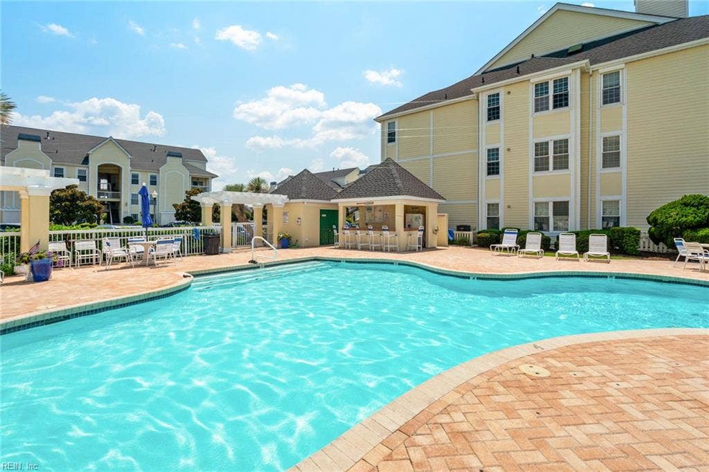 Community pool with paver deck, lounge chairs, pergola seating, and a covered cabana with bar seating and outdoor shower at Lesner Pointe in Chic's Beach, Virginia Beach. Pool access comes with this first-floor 3 bedroom condo. 23451.