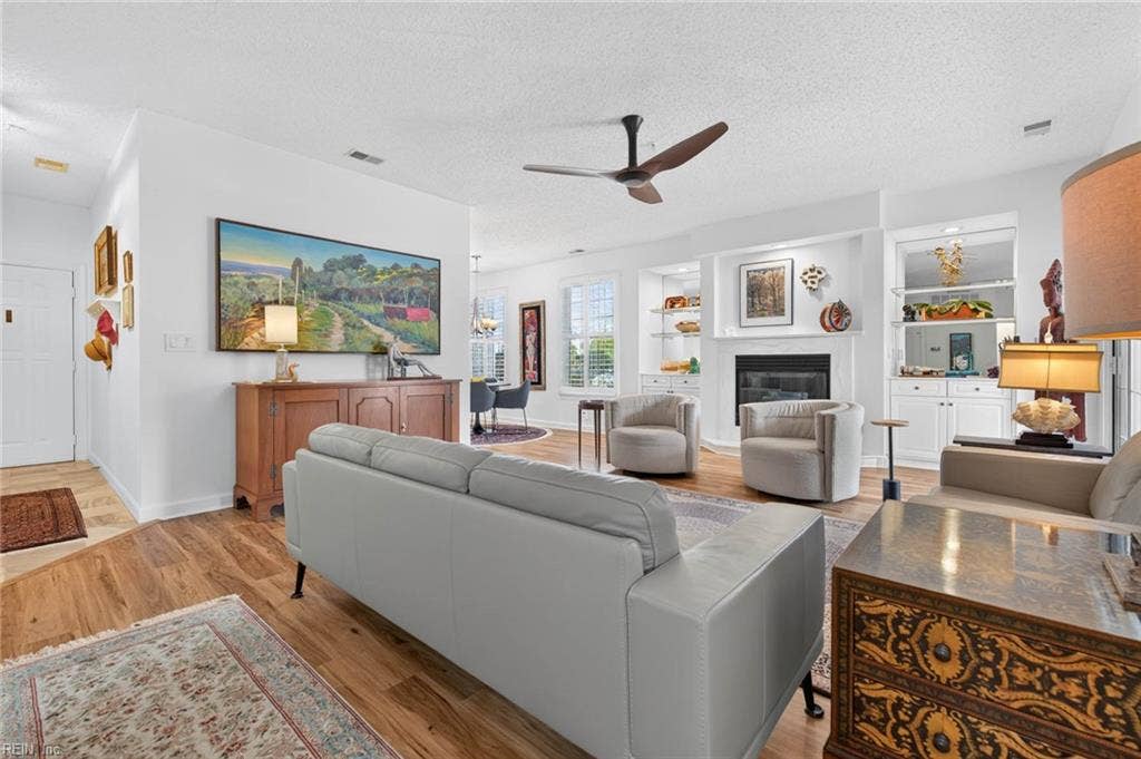 Open floor plan connecting the entry, living room, dining area, and kitchen, with LVP flooring in the main living space. Gas fireplace and ceiling fan in this 1995 first-floor condo at Lesner Pointe, Virginia Beach. 23451.