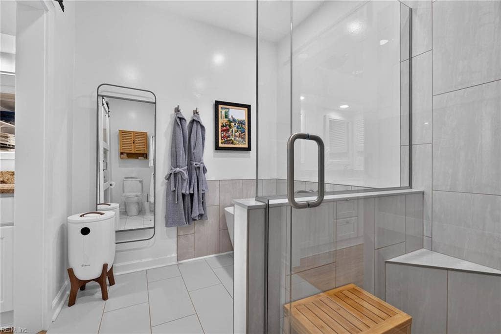 Primary bathroom with glass-enclosed tile shower with corner bench and pebble shower floor, large-format tile bathroom floor, and separate toilet room. Gutted and renovated by current owners. Lesner Pointe condo, Chic's Beach, Virginia Beach. 23451.