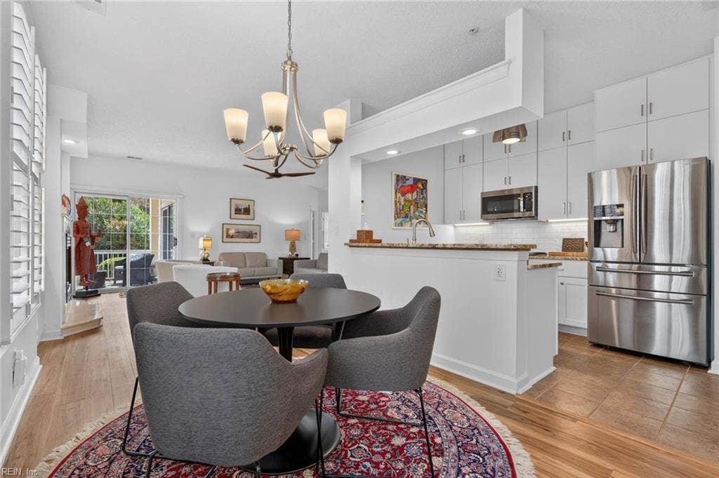Dining area between the kitchen and living room with a chandelier and LVP flooring, with the sliding glass door to the patio in view. Open layout in this Lesner Pointe first-floor condo, Chic's Beach, Virginia Beach.