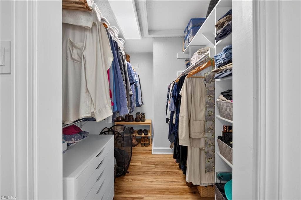 Primary walk-in closet with double hanging rods, built-in shelving, drawer unit, and LVP flooring. Closet connects to the primary bedroom and bath in this 3 bedroom, 2 bath Lesner Pointe condo, Chic's Beach, Virginia Beach.