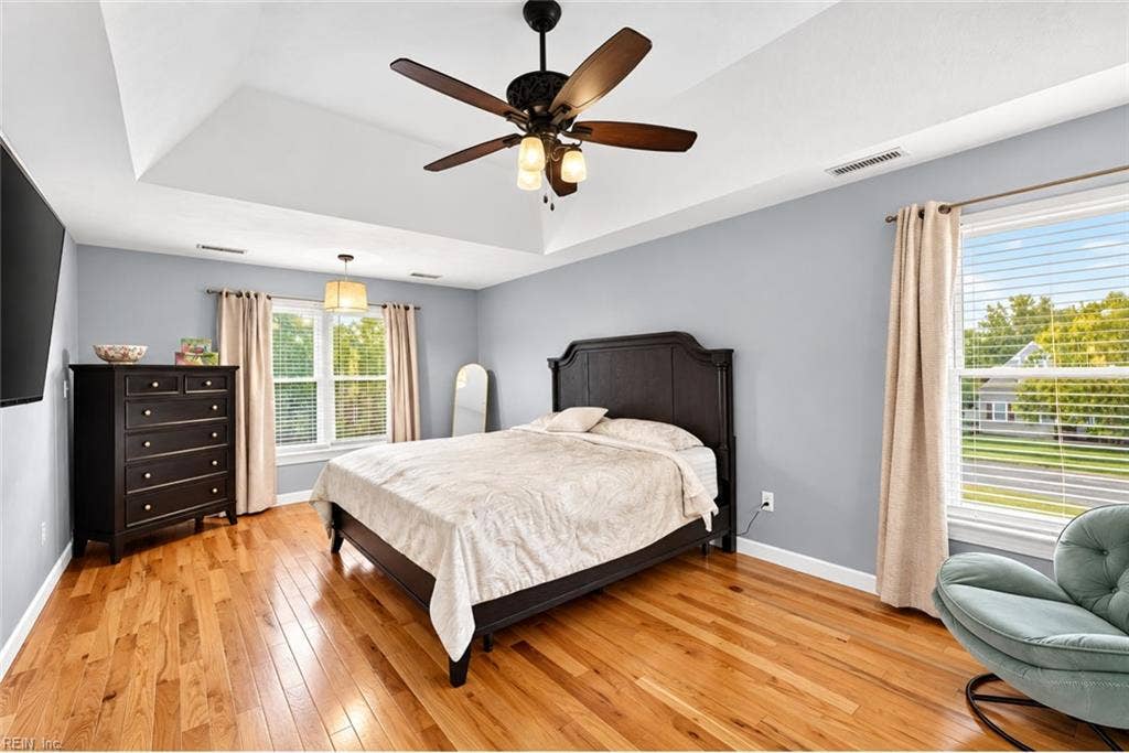 Spacious primary bedroom with multiple windows and hardwood flooring