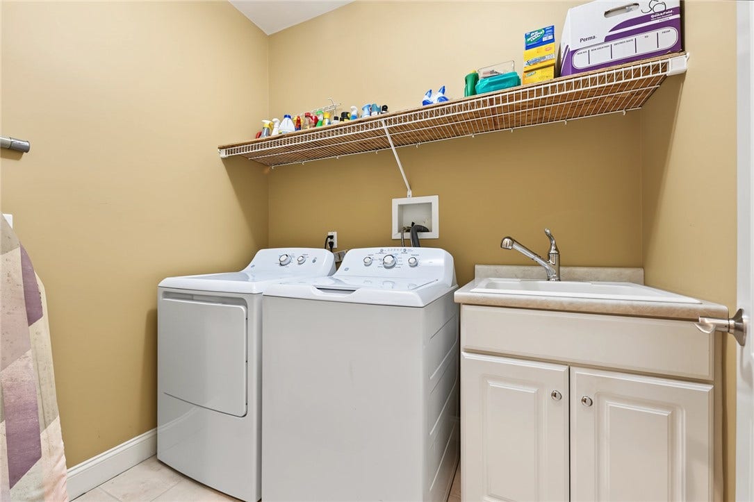 95 Fry Brook Drive, East Greenwich, RI 02818 Located just outside the two bedrooms, this laundry room features a full-size washer and dryer, utility sink with storage cabinetry, and generous shelving for laundry and household essentials.