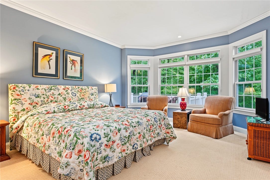 95 Fry Brook Drive, East Greenwich, RI 02818 A spacious primary suite featuring a graceful tray ceiling and an impressive wall of windows that fills the room with natural light while framing serene wooded views.