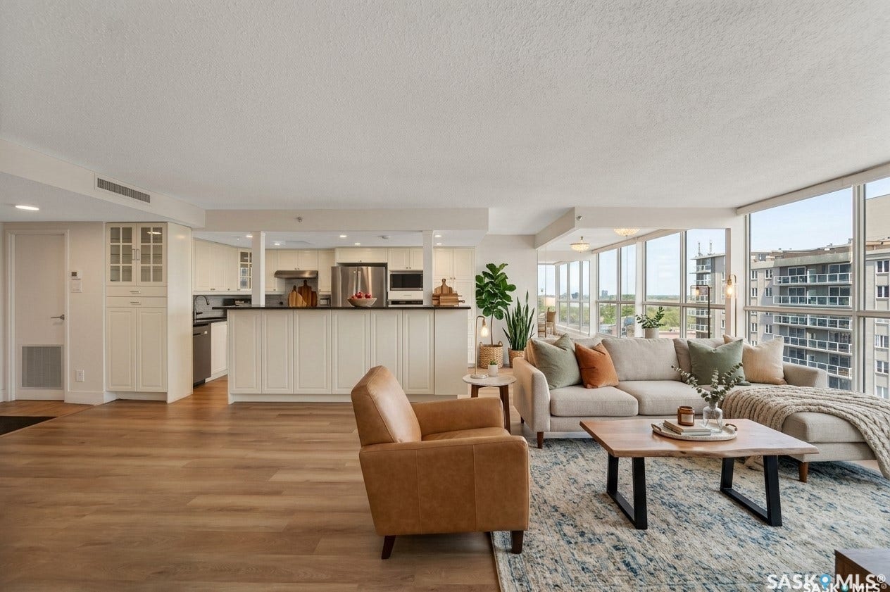 Open-concept living area with wood-finish flooring, full-height windows, and a built-in kitchen island featuring white cabinetry and a dark countertop
