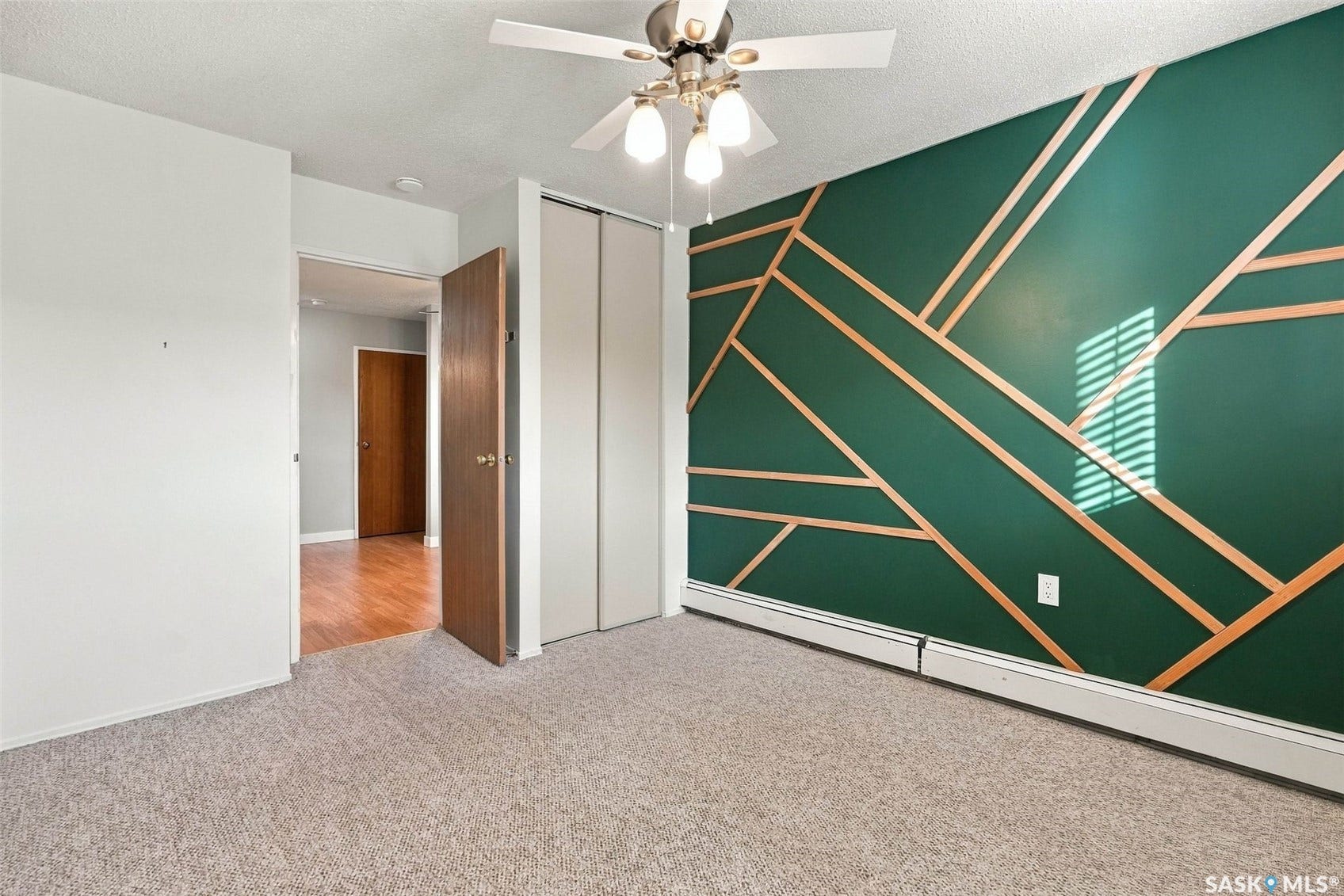 3410 Park Street, #119, Regina SK S4V 2M8 Feature wall with geometric wood paneling, ceiling fan with light fixture, carpet flooring, and bi-fold closet doors